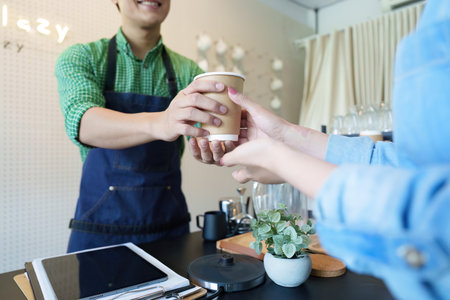 Sustainability and Enjoying Coffee. A barista hands a customer a coffee in a sustainable cup, emphasizing eco-conscious consumption.の写真素材