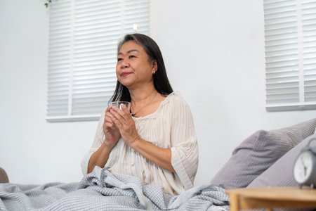 Morning Routine and Relaxation. An elderly woman seated comfortably in bed, enjoying a warm beverage.の写真素材