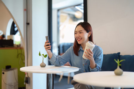 Leisure and Relaxation. A young customer enjoys her coffee while using her phone in a cozy cafe...