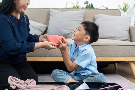 Packing and Family Bonding. A joyful boy helps his mother pack for a family trip, sharing smiles and excitement.の写真素材