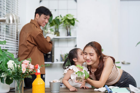 A joyful moment between a mother and her daughter as they bond over caring for plants, with a family member joyfully assisting.の写真素材
