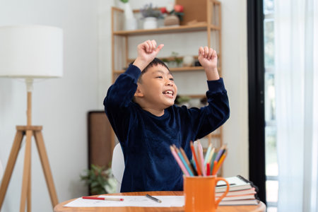 Achievement and Learning. A young boy celebrates his success while studying at home, showcasing excitement for learning.の写真素材