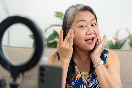 Skincare Application and Elderly Empowerment. A senior woman smiling while applying skincare products during a video session.の写真素材