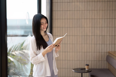 Reading and Joy. A young woman immersed in her book, smiling in a cozy cafe.の写真素材