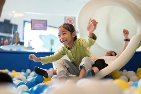 Exciting Slide Adventure. Happy girl sliding down into colorful ball pit, expressing joy and excitement.の写真素材