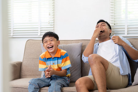 Father and Son Laughing Together. A playful moment shared on the couch.の写真素材