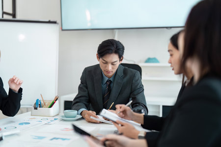 Focused Asian business executive leading a strategy meeting with colleagues in a modern conference room.の写真素材