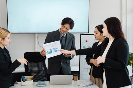 Diverse business team analyzing financial graphs and discussing strategies in a modern office.の写真素材