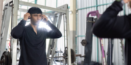 Gym Preparation. Man adjusting headphones while looking in the mirror at the gym.