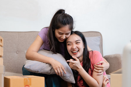 Diverse female couple sharing a joyful moment while embracing on the couch during their move.の写真素材
