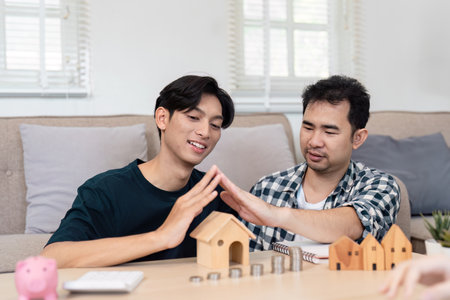 LGBTQ couple forming a house symbol with their hands while planning savings for a future home together.の写真素材