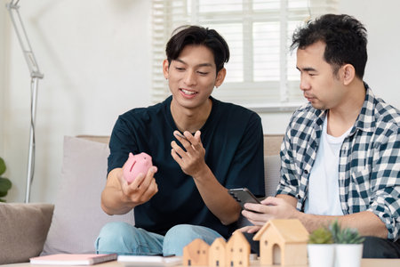 Loving LGBTQ couple discussing savings strategies while sitting on a couch at home. Financial planning and budgeting for a secure future in a cozy living space.の写真素材