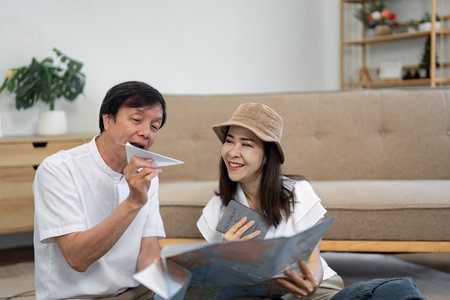 Elderly Asian couple joyfully exploring a travel map and discussing plans while holding a passport,...