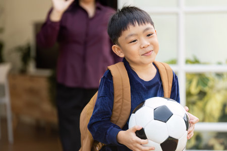 Back to School and Family Bonding. A young boy with a soccer ball smiles as his parent prepares him for school.の写真素材