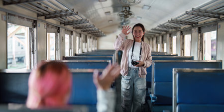 Travel and Friendship. A woman joyfully waving at her friend while capturing memories in a vintage train setting.の写真素材