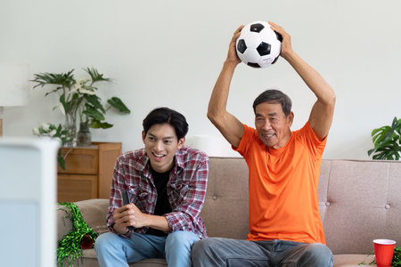 Family Bonding During Soccer Game. A young man and his father celebrating together while watching soccer at home.の写真素材