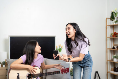 Friendship and Fun. Two young women enjoying music and laughter in a cozy living room.の写真素材