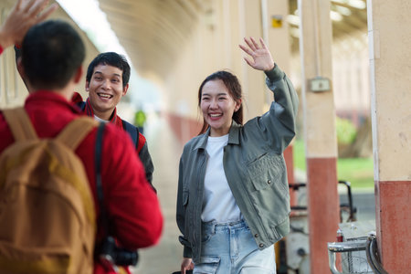Joyful Reunion. Young adults greeting each other with smiles and waves at a train station.の写真素材