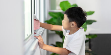 Cleaning and Learning. A young boy cleans a window, learning responsibility and hygiene at home.の写真素材
