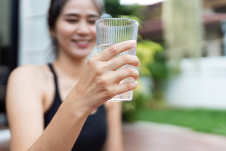 Wellness and Hydration. Young woman enjoying a refreshing glass of water outdoors.の写真素材