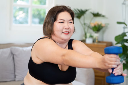Inclusive Wellness. Plus-size woman exercising with dumbbell at home.の写真素材