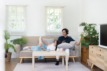 Couple enjoying cozy time at home, relaxing on sofa with technologyの写真素材