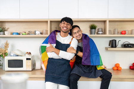 LGBT couple embracing with pride flag in the kitchen. Celebrating love and diversity.の写真素材
