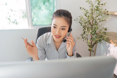 Remote Work. Young woman on phone and headset multitasking in home office.