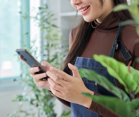 Remote Work. Young woman smiling while texting on her phone in a plant-filled workspace.