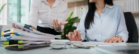 Office Discussion. Two women engaged in a conversation about project documents in a modern...