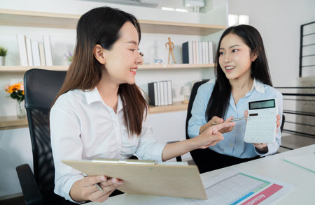 Financial Consultation. Two women analyzing data with a calculator in a professional setting.の写真素材