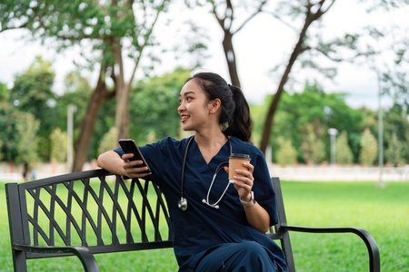Doctor smiling while using smartphone on park benchの写真素材