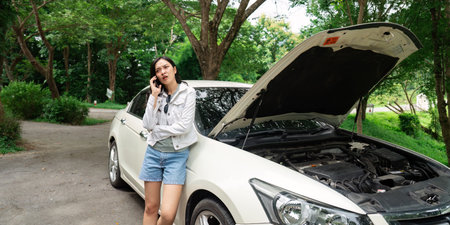 Car Trouble. A young woman on the phone while her car hood is open, seeking help.の写真素材