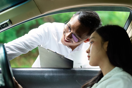 Insurance Consultation. A man smiling while discussing car insurance with a woman in a vehicle.の写真素材