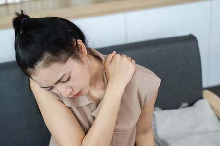 Physical Health. Young woman experiencing shoulder pain while seated indoors.