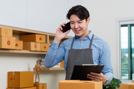 E-commerce professional on phone. A man in an apron discussing logistics while managing packages.の写真素材