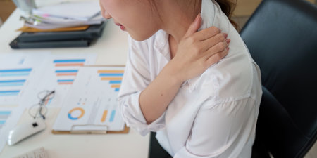 Neck Pain Relief. Young woman experiencing shoulder discomfort while working at a desk.の写真素材