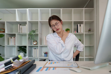 Workplace Strain. Young woman holding shoulder in discomfort while working at desk.
