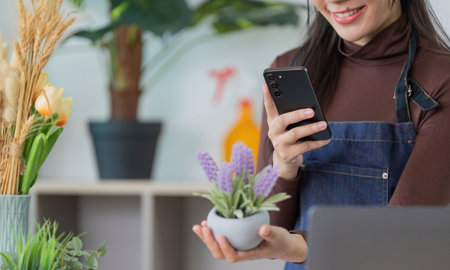 Customer Engagement. Woman holding a plant while checking her smartphone.の写真素材