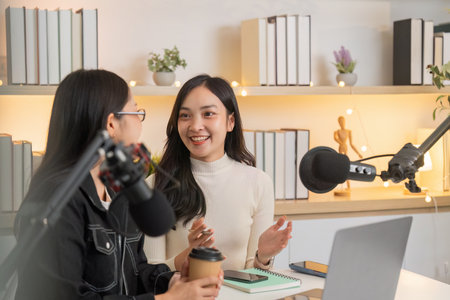 Podcast Discussion. Two women engaging in a lively conversation in a modern studio.の写真素材