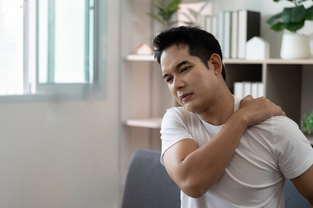 Shoulder Pain. Young man feeling discomfort in shoulder while seated.の写真素材