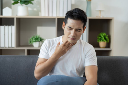 Health Alert: Man feeling throat discomfort in a modern living spaceの写真素材