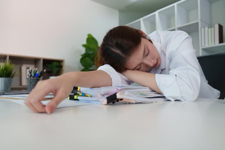 Exhausted young woman resting on paperwork in office