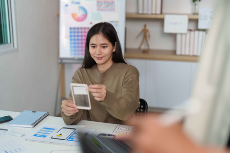 UI UX Design Collaboration. Young woman showcasing smartphone prototype in creative workspace.の写真素材