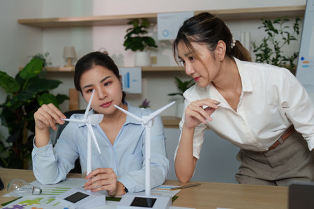 Collaborative Strategy. Women discussing wind turbine models and ESG initiatives in office.