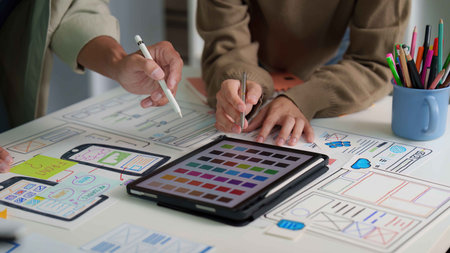 User Interface Design. Team discussing digital mockups and color palettes on a tablet.