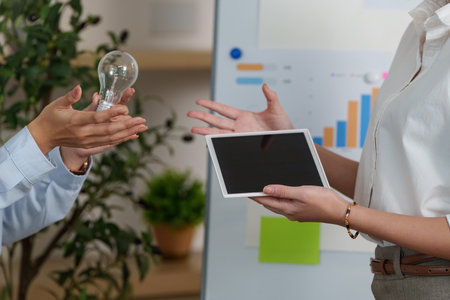 Innovative ESG Solutions. Professional discussing sustainable ideas with a light bulb and tablet.