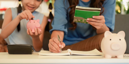 Teaching Financial Skills. Mother and daughter saving money with piggy banks.の写真素材