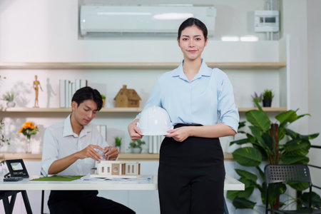 Sustainability in Architecture. Female architect holding hard hat with male colleague working.の写真素材