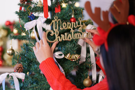 Holiday Cheer. Young girl placing a festive ornament on a Christmas tree with a joyful expression.の写真素材